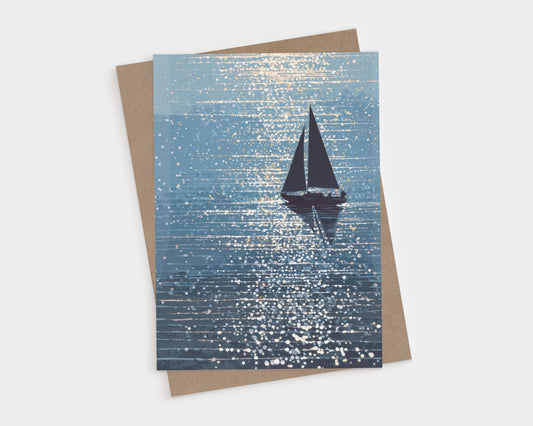 Greeting card featuring a silhouetted sailboat gliding across shimmering blue water, with sparkling sunlight scattered across the waves. The artwork has a dreamy, painterly style with rich navy and soft aqua tones. A kraft envelope is partially visible behind the card.