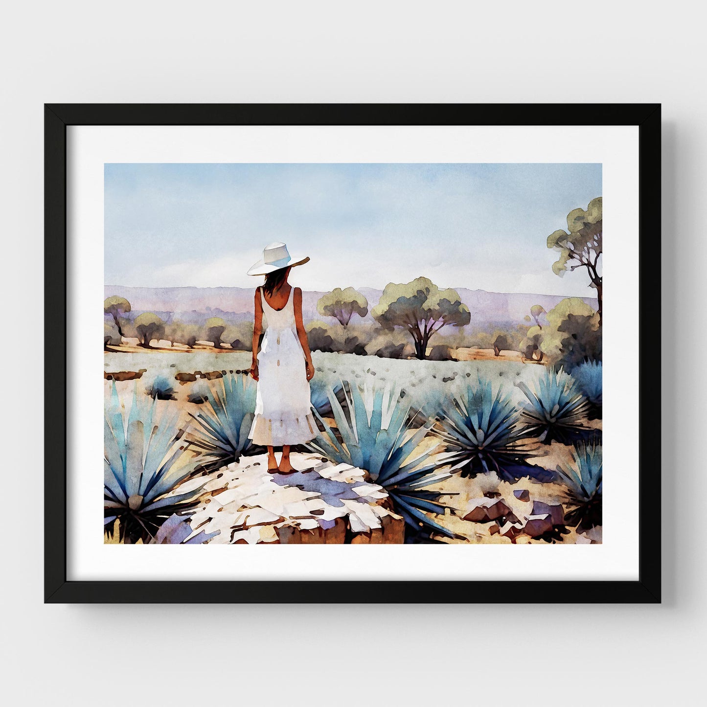 Black framed artwork of a woman in a white dress and hat standing in an agave field.