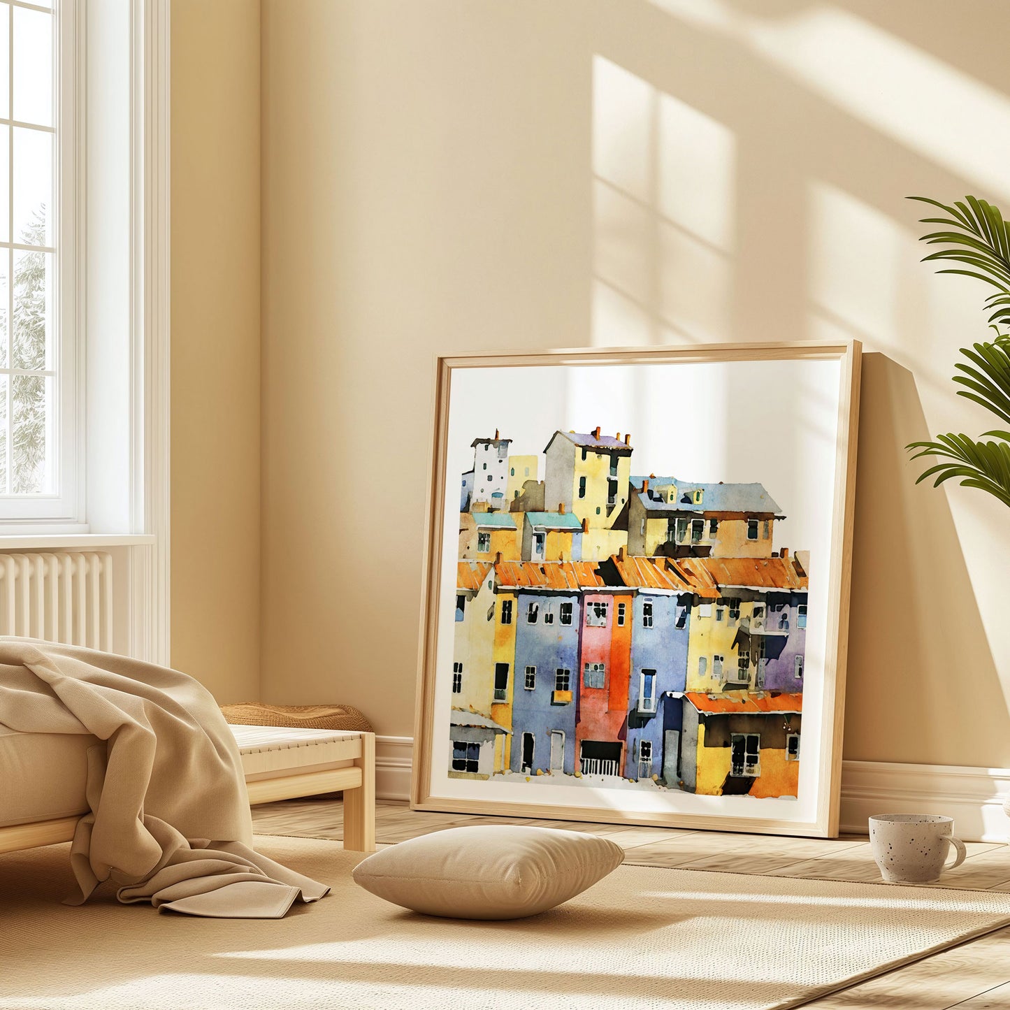 Framed watercolor painting of a colorful hillside village with vibrant buildings, placed on the floor in a cozy, sunlit bedroom.