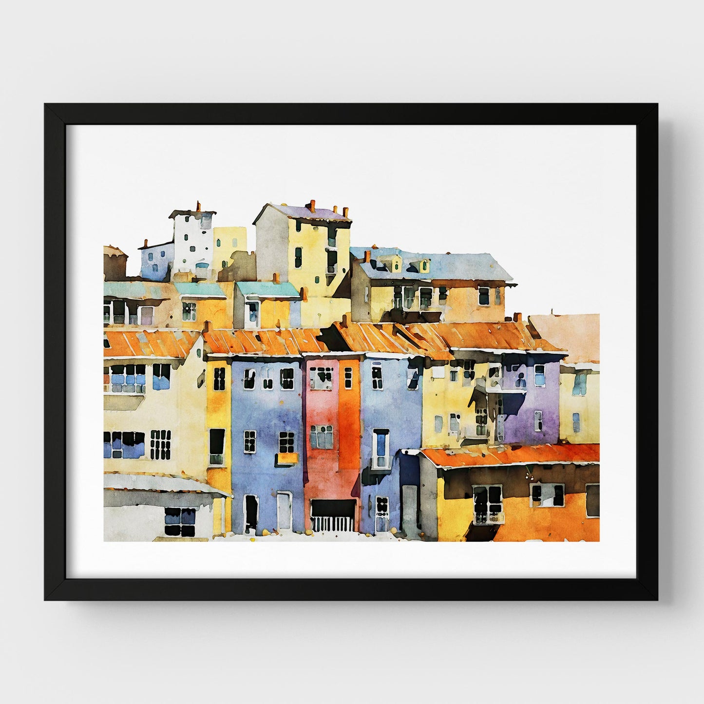 Framed watercolor painting of a colorful hillside village with vibrant buildings, mounted on a white wall with a black frame.