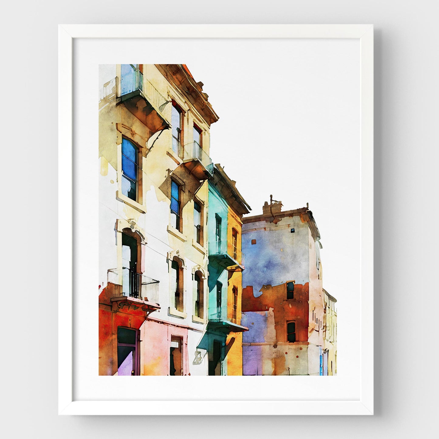 Framed watercolor painting of colorful buildings with pastel facades, mounted on a white wall with a white frame.