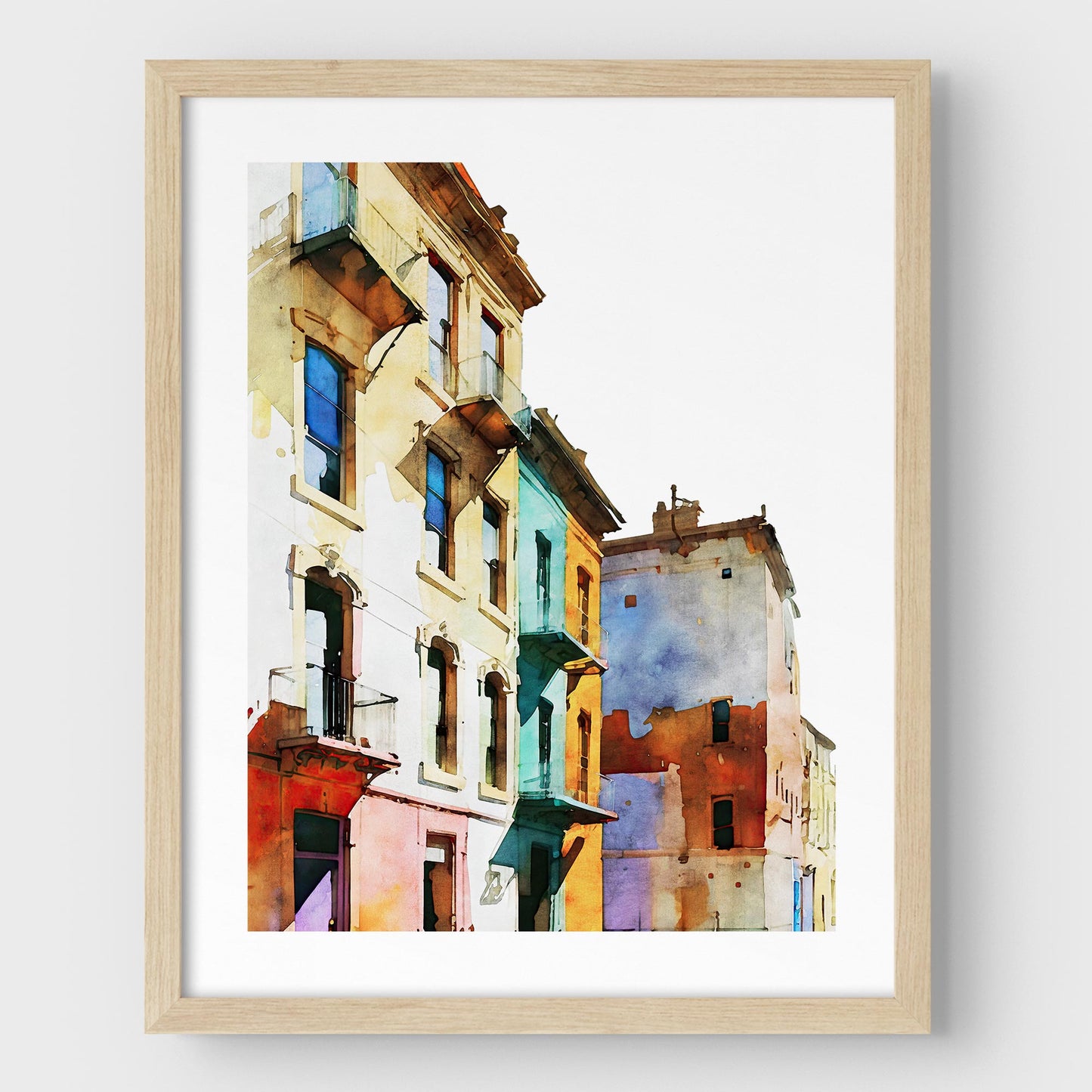 Framed watercolor painting of colorful buildings with pastel facades, mounted on a white wall with a natural wood frame.