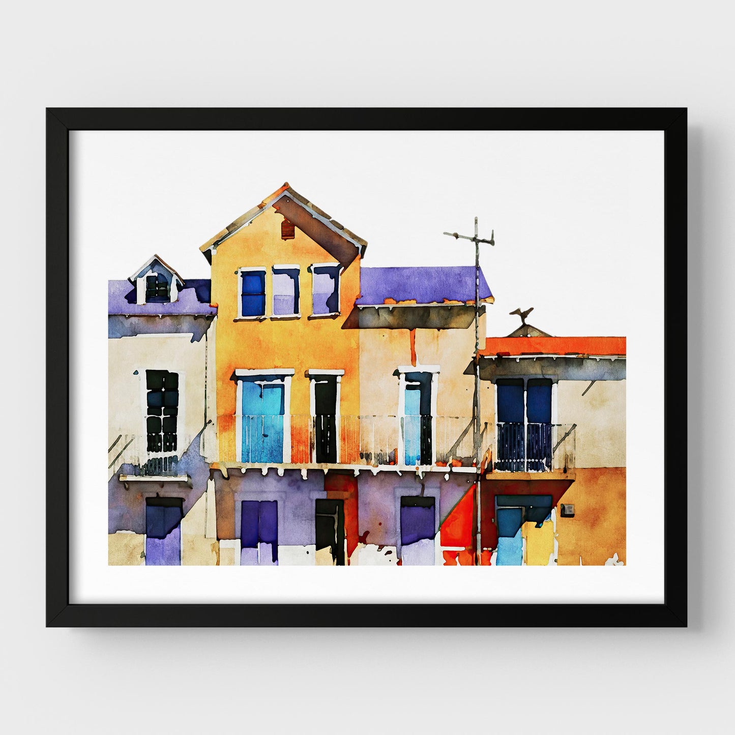 Framed watercolor painting of colorful buildings with blue, yellow, and purple facades, mounted on a white wall with a black frame.