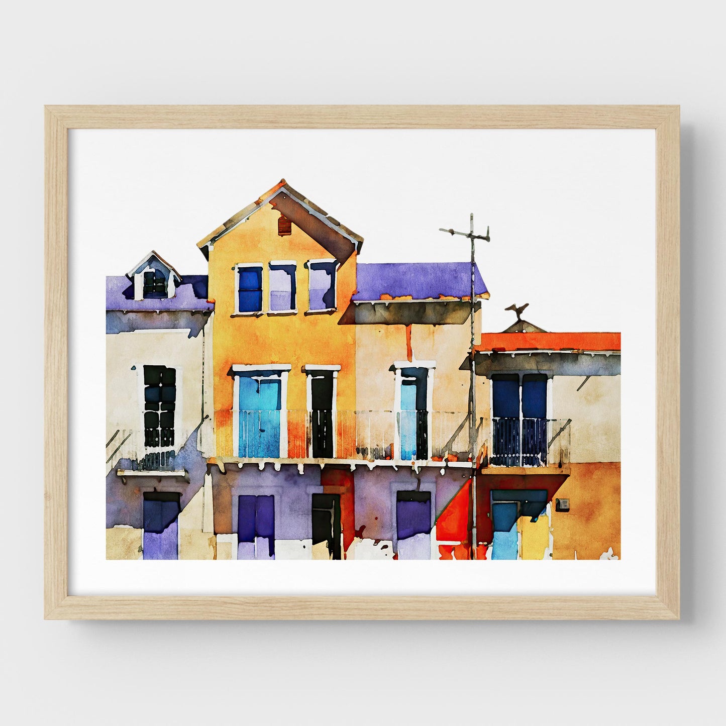 Framed watercolor painting of colorful buildings with blue, yellow, and purple facades, mounted on a white wall with a natural wood frame.