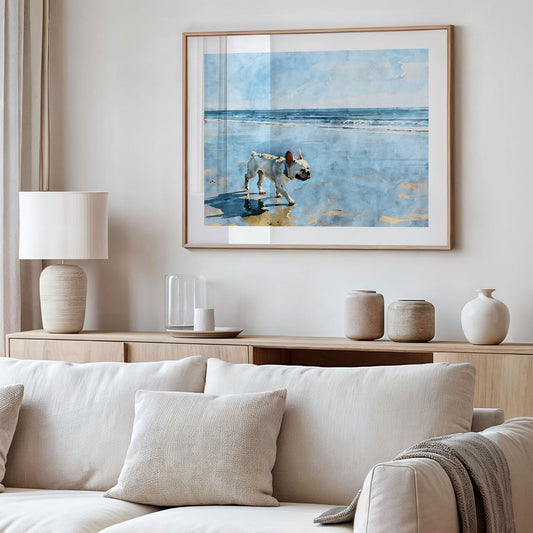 Framed cream French Bulldog beach watercolor art displayed in a styled interior with soft blue and sandy neutral tones.