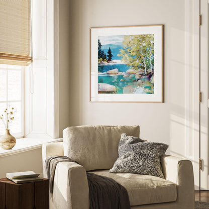Framed landscape painting of a turquoise lake with rocks, trees, and distant mountains hangs on a neutral wall above a beige armchair. The cozy corner features a textured gray pillow, dark throw blanket, wooden side table with a book, and a ceramic vase with dried flowers on the windowsill, softly lit by natural light.