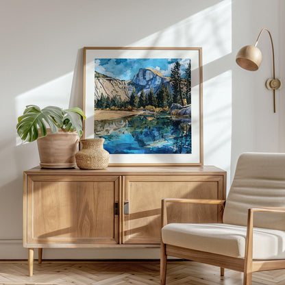 Framed art print of Yosemite’s Half Dome with pine trees and a mirrored river, painted in a bold modern watercolor style. The artwork is displayed on a wooden sideboard in a bright, minimalist living room, accented with a potted plant, woven vase, cream armchair, and natural light streaming across the wall.