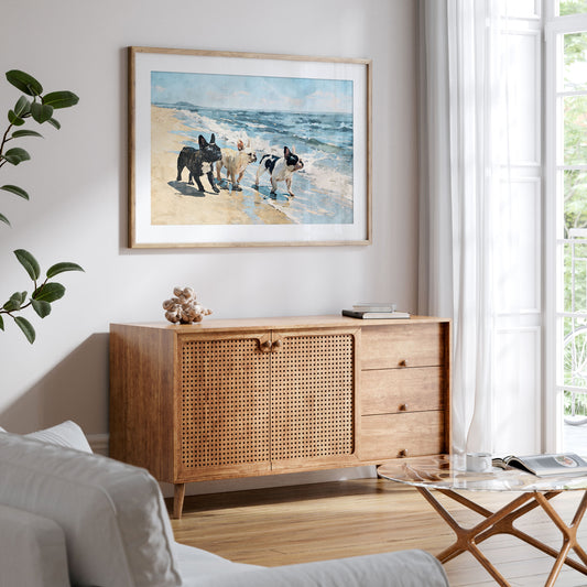 Framed watercolor art of three French Bulldogs walking on a beach displayed in a styled interior with blue and tan coastal tones.
