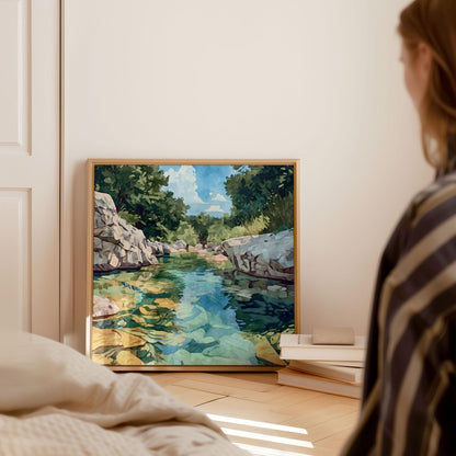 Framed watercolor-style painting of a clear rocky river with turquoise and green water, leaning against a wall beside stacked books in a softly lit bedroom. A woman in striped clothing sits nearby, gazing at the artwork, with sunlight streaming across the wooden floor.
