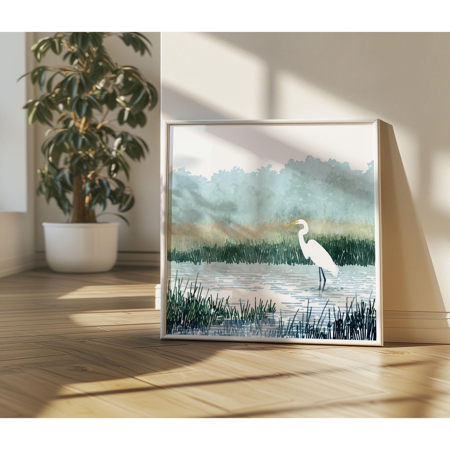 Framed watercolor-style print of a white heron standing in a marsh, resting against a sunlit wall on a wooden floor, with soft shadows and a potted tree in the background.