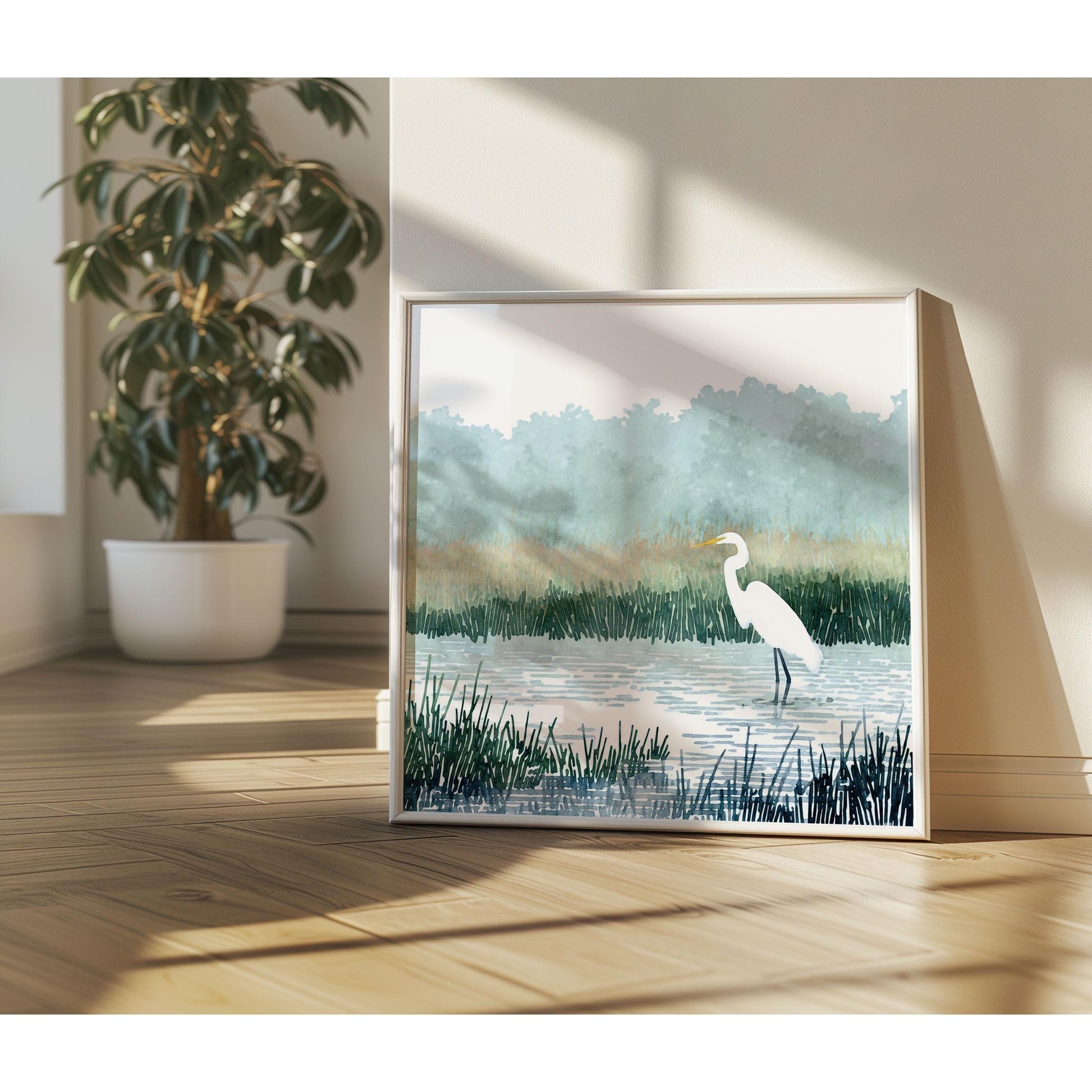 Framed watercolor-style print of a white heron standing in a marsh, resting against a sunlit wall on a wooden floor, with soft shadows and a potted tree in the background.