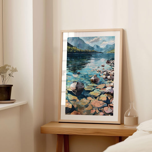 Framed watercolor painting of a tranquil lake with clear blue water, colorful submerged rocks, and a distant view of pine-covered mountains under a partly cloudy sky, displayed on a wooden table in a softly lit bedroom.