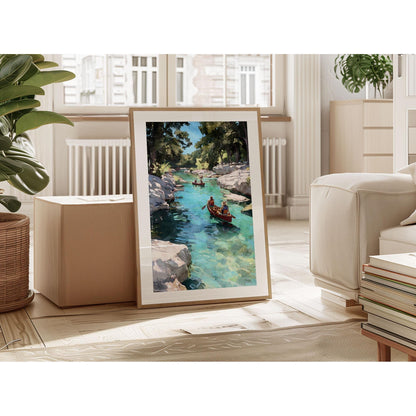 Framed painting of two people canoeing on a turquoise river surrounded by rocky cliffs and trees, displayed leaning against a wall in a bright, modern living room with plants, books, and natural light from large windows.