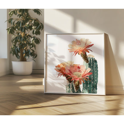 Watercolor cactus art print with large peach and coral blooms, displayed in a white frame leaning against a wall, bathed in warm sunlight beside a potted plant on wooden floors.