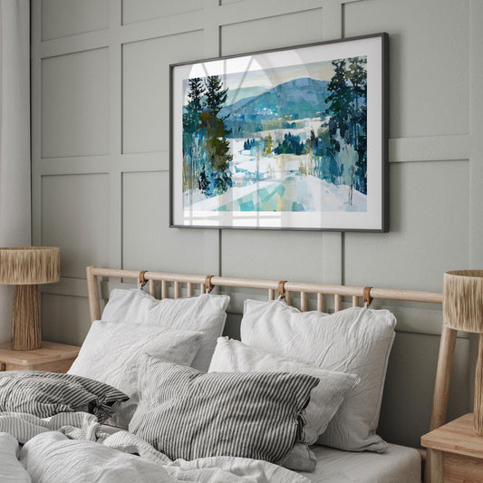 Framed winter landscape painting featuring snow, evergreen trees, and blue-green mountains, displayed above a bed with white linens and striped pillows in a modern, neutral-toned bedroom with wood accents and soft natural light.