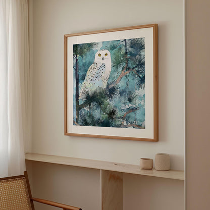 Framed watercolor-style art print of a snowy owl with bright yellow eyes perched among pine branches, in cool blue and green tones. The artwork hangs on a light neutral wall above a minimalist wooden ledge with two small ceramic vessels, next to a woven chair and soft white curtains.