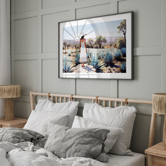 A bedroom with a sage green paneled wall features a framed artwork of a woman in an agave field above a bed with white and striped pillows.