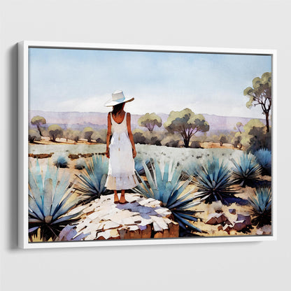 White framed canvas print of a woman in a white dress and hat standing on a rock in an agave field with trees and mountains in the background.