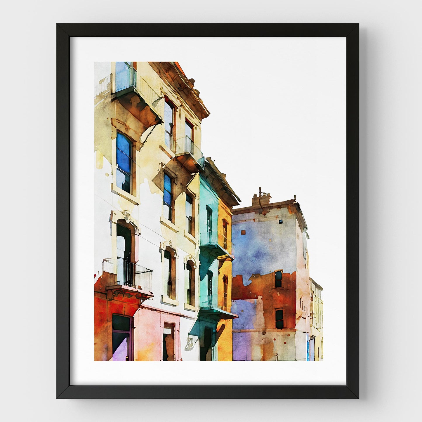 Framed watercolor painting of colorful buildings with pastel facades, mounted on a white wall with a black frame.