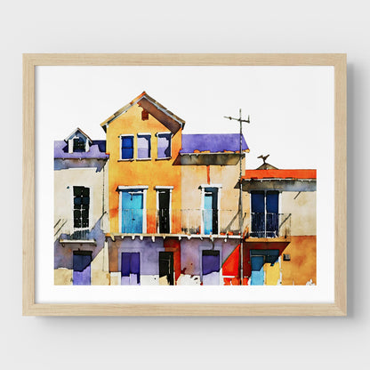 Framed watercolor painting of colorful buildings with blue, yellow, and purple facades, mounted on a white wall with a natural wood frame.