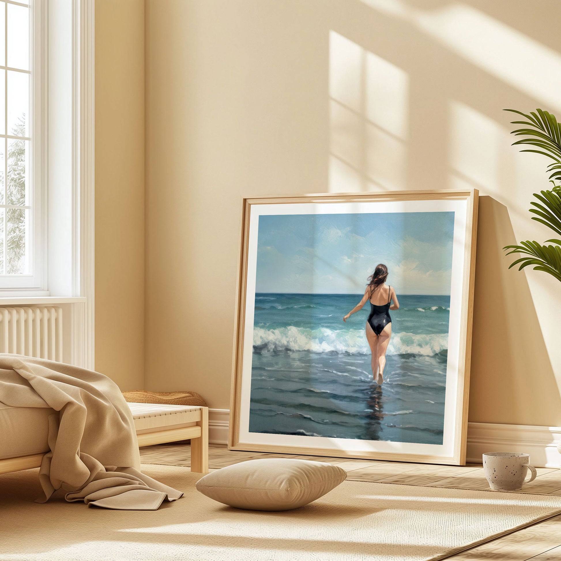 Framed painting of a woman in a black swimsuit walking into the ocean, leaning against a wall in a sunlit, beige-toned room with a pillow and blanket nearby.