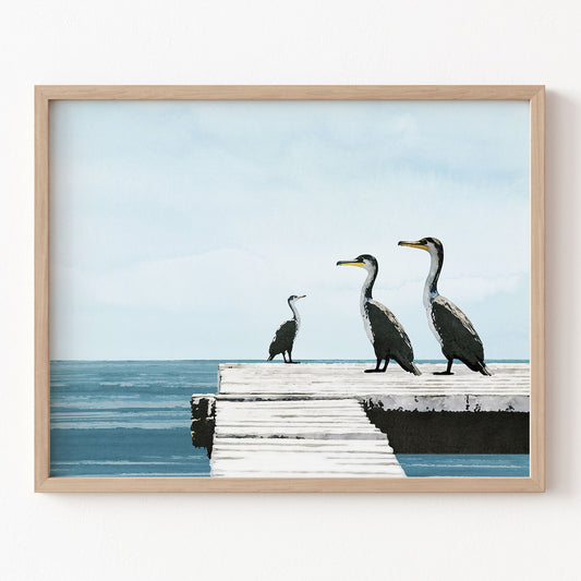 Framed artwork of three birds on a dock with a blue sky and water background.
