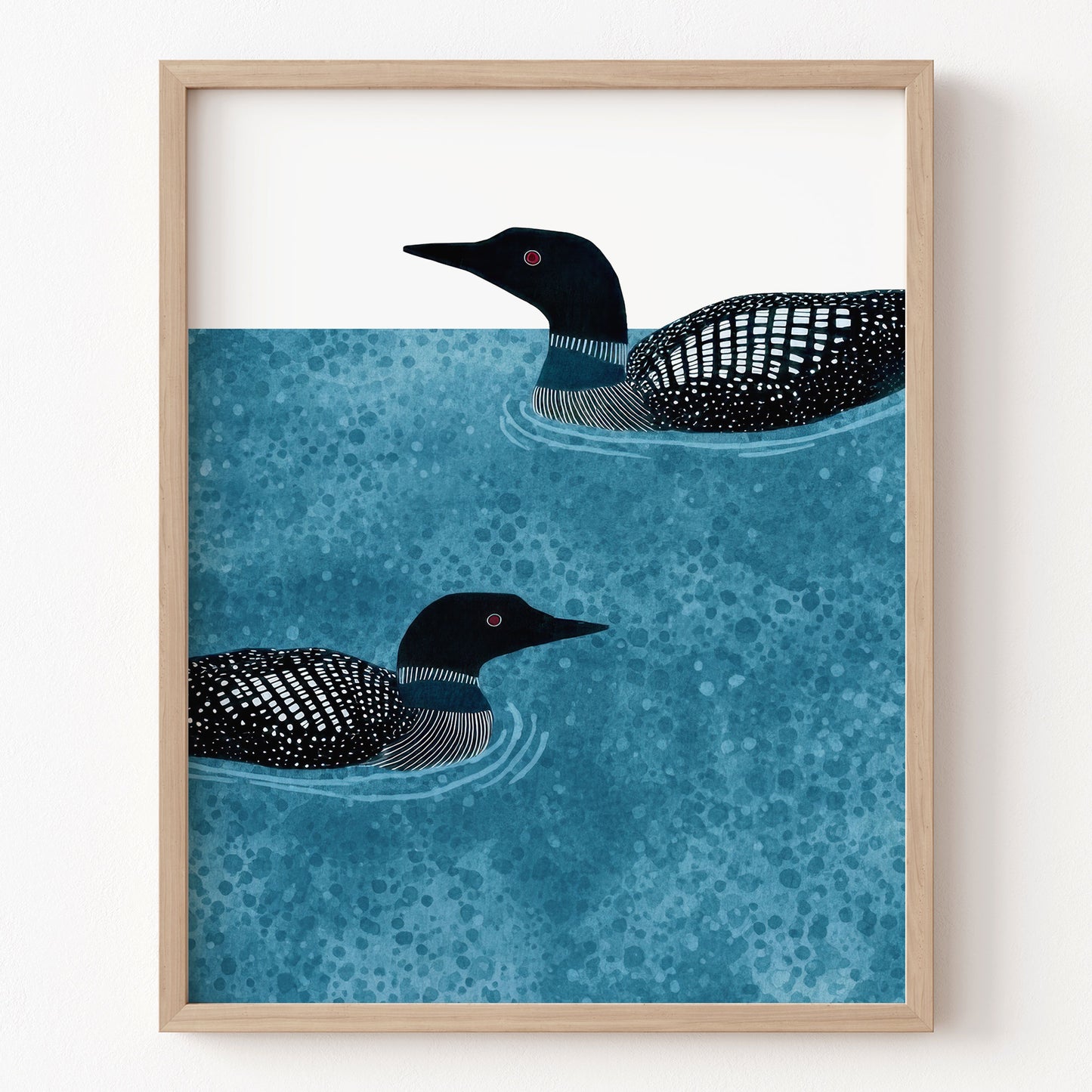 Framed artwork of two loons swimming on water with a wooden frame.