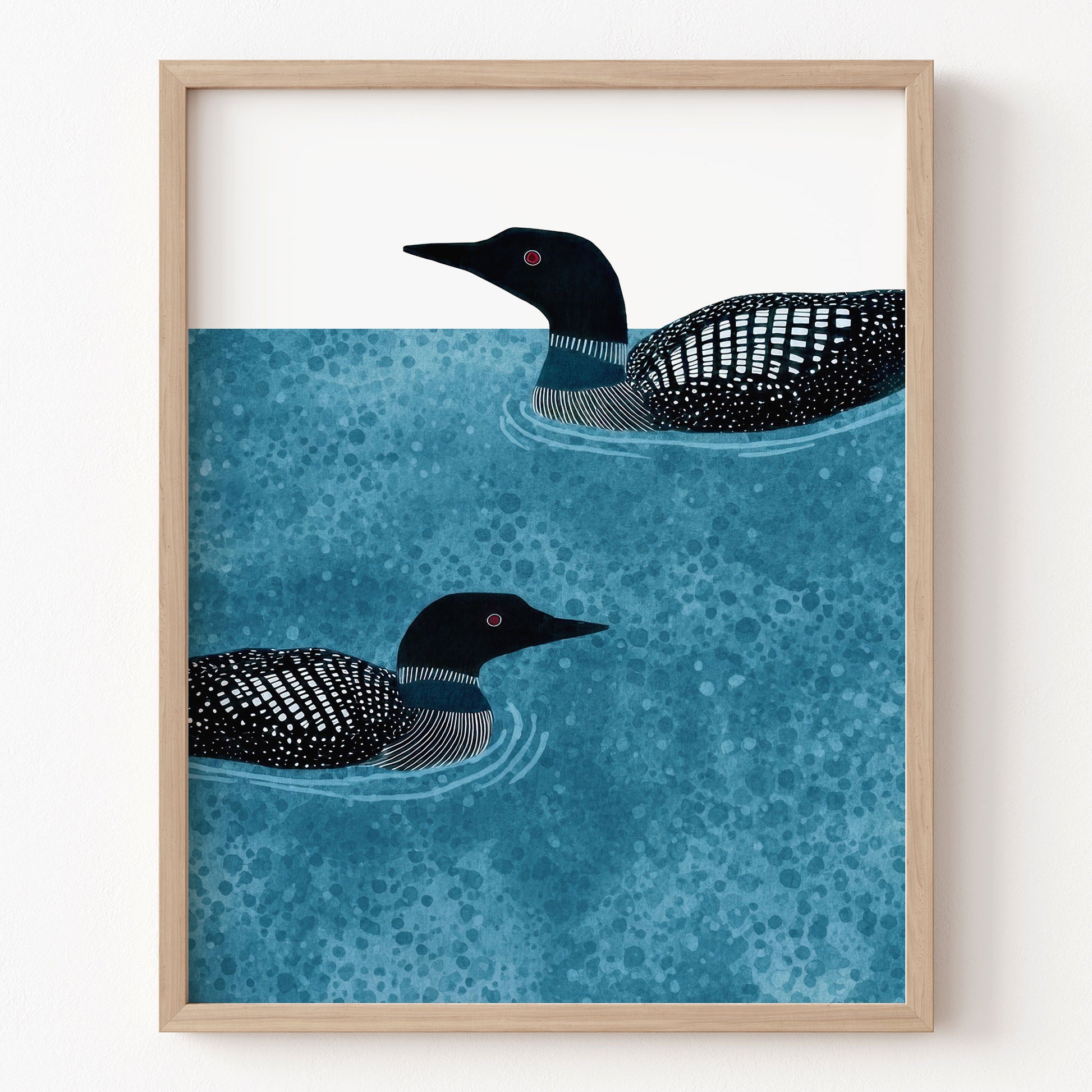 Framed artwork of two loons swimming on water with a wooden frame.