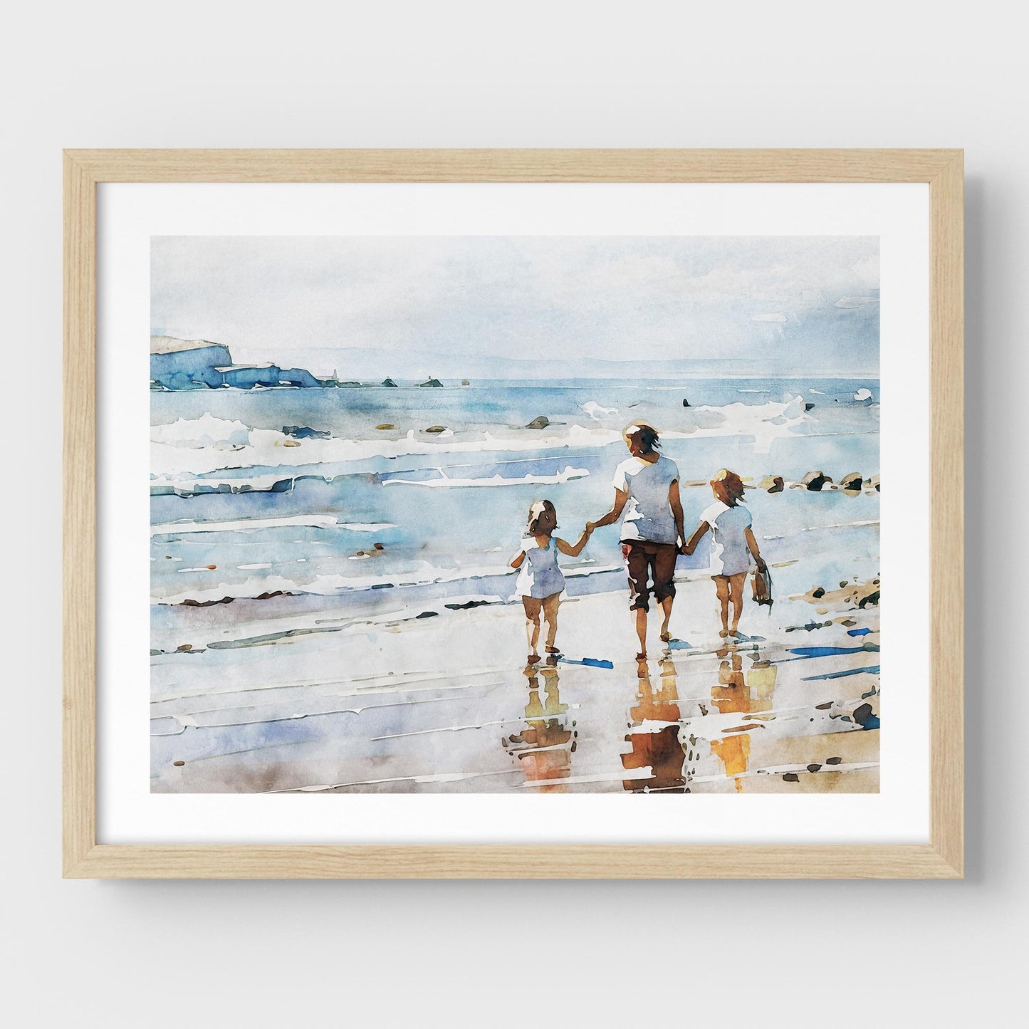 Framed watercolor painting of a woman and two children walking along the shoreline, mounted on a white wall with a natural wood frame.