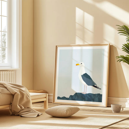 Framed illustration of a seagull on a dark blue rock, leaning against a beige wall in a sunlit room with warm neutral decor and a floor cushion.