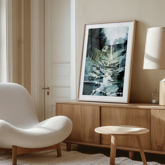 Framed watercolor painting of a cascading waterfall, placed on a wooden sideboard in a cozy, neutral-toned room with a modern chair.