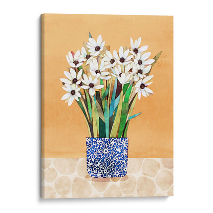 Canvas artwork of white flowers with dark centers in a blue patterned vase, displayed on a patterned beige surface against an orange backdrop.