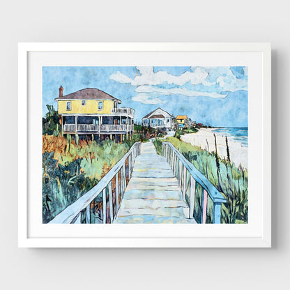 White framed watercolor-style artwork depicting a sunny coastal boardwalk leading to a row of colorful beach houses, with a bright yellow home in the foreground, lush dune grasses on either side, and the ocean visible on the right.