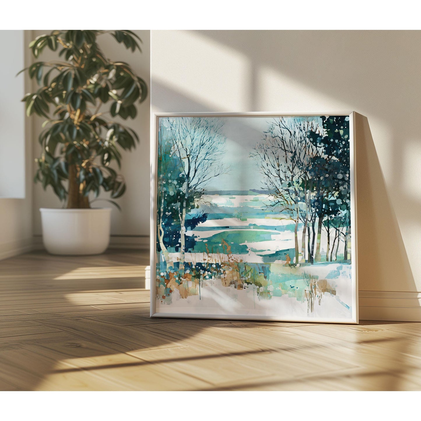 Framed watercolor winter landscape featuring bare trees, evergreens, and a snow-dappled field in teal, blue, and white hues, leaning against a sunlit wall with a potted plant nearby on wooden flooring.