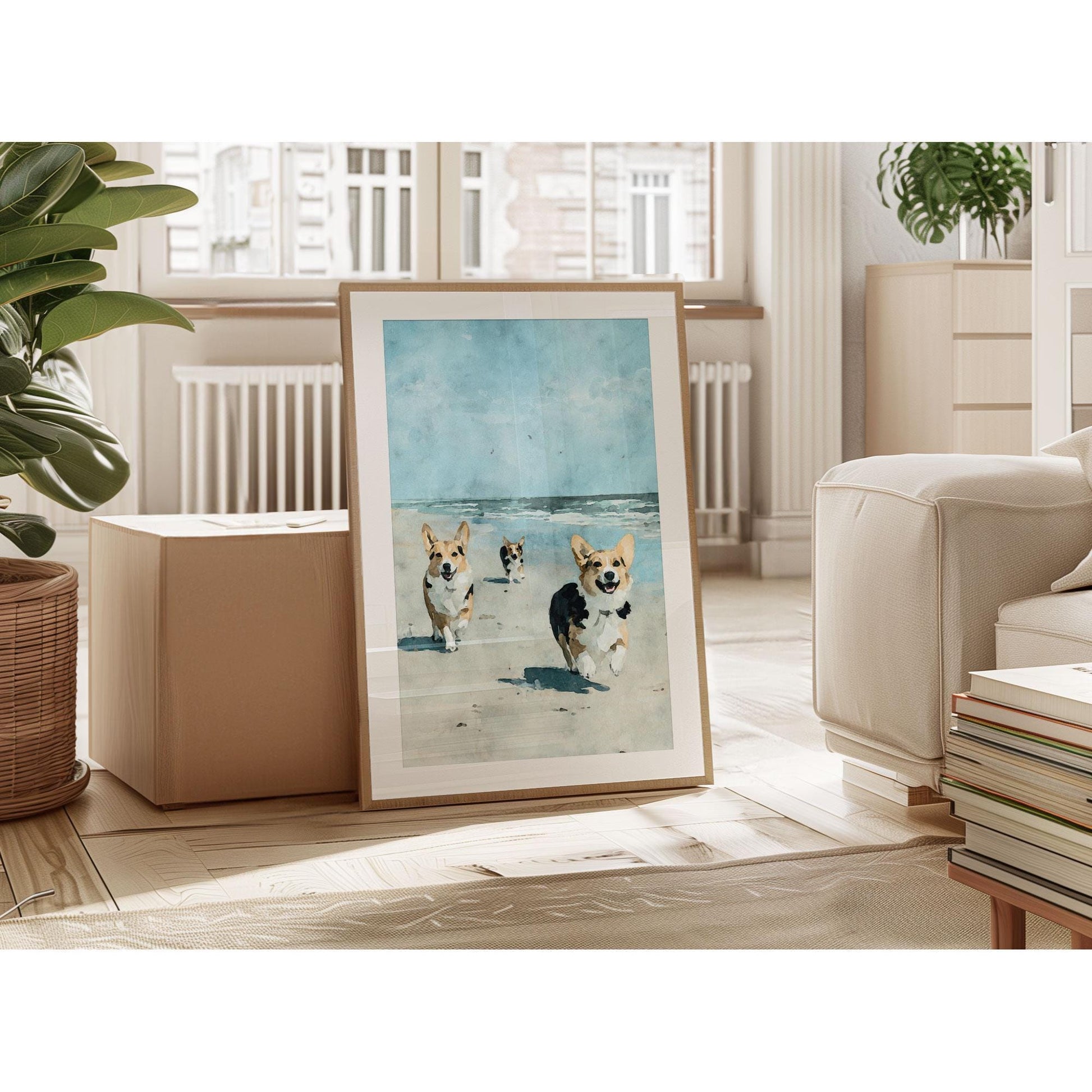 Framed painting of three corgis running on a sandy beach with ocean waves and a blue sky, leaning against a wall in a bright living room with plants, books, and neutral-toned furniture.