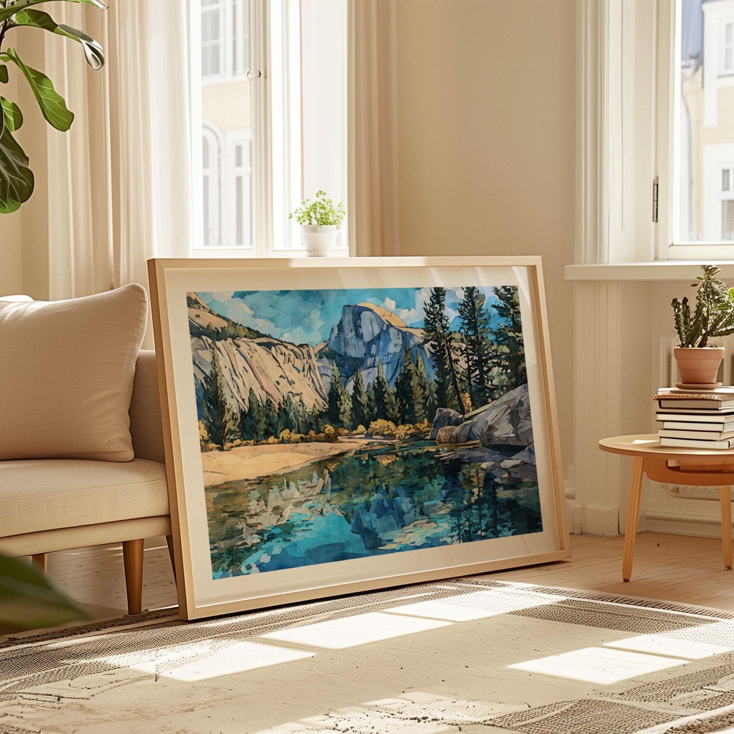 Large framed art print of Yosemite’s Half Dome with pine trees and a reflective river, painted in bold modern watercolor style. The artwork leans against a wall in a sunlit living room, placed beside a cream sofa and a small wooden table with books and a potted plant. Neutral tones and natural light create a cozy, modern atmosphere.